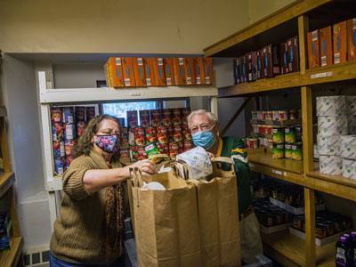 Two church members standing in pantry bagging up groceries for those in need